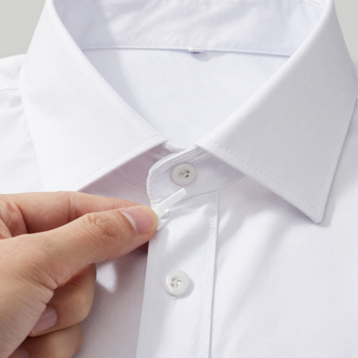 Thin collar stay being slid into the channel on the underside of a shirt collar point